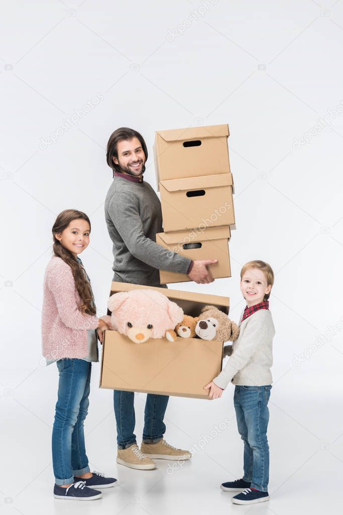 Happy children holding cardboard box with toys while father carrying stack of boxes isolated on white 