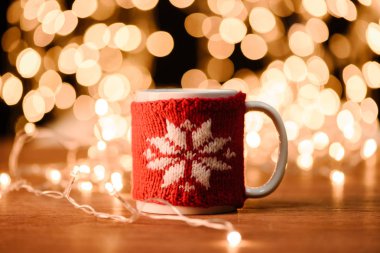 close up view of cup of hot drink and garland on wooden tabletop with bokeh lights background clipart