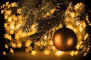 close up view of golden christmas ball hanging on pine tree with stars bokeh lights background clipart
