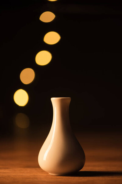 close up view of white vase and yellow bokeh lights on black background