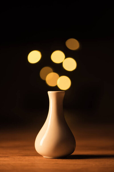 close up view of white vase and yellow bokeh lights on black background