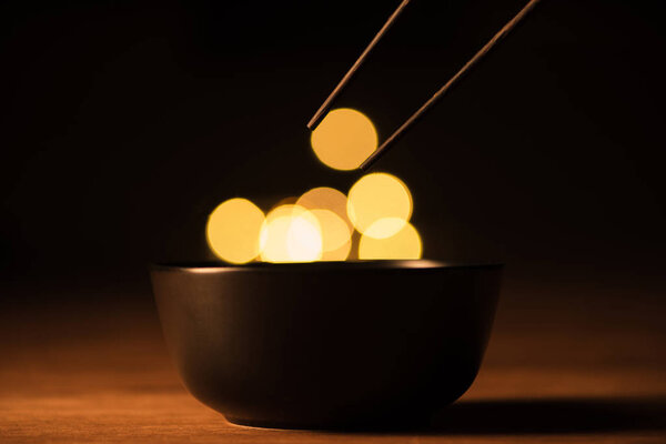 close up view of bowl, chopsticks and bokeh lights on black background