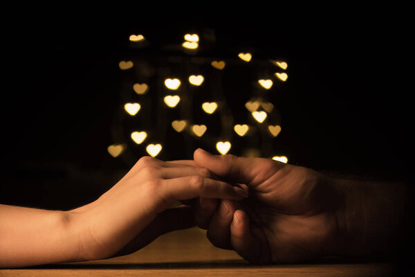 cropped shot of couple holding hands with hearts bokeh background