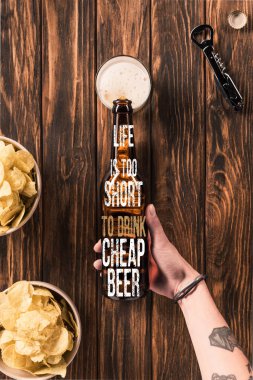 cropped image of woman pouring beer into glass at wooden table with crispy chips, with 