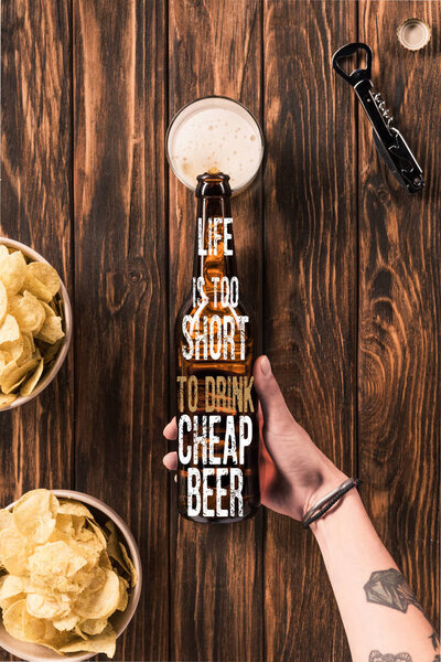cropped image of woman pouring beer into glass at wooden table with crispy chips, with "life is too short to drink cheap beer" inspiration