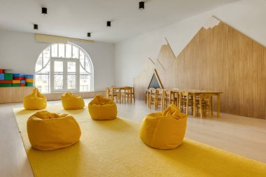 yellow bean bag chairs and wooden tables in kindergarten playing room clipart