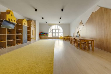cozy kindergarten classroom interior with yellow carpet, tables and tv clipart
