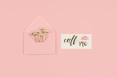 top view of open pink envelope with small white flowers, card with call me inscription and kiss mark isolated on pink clipart
