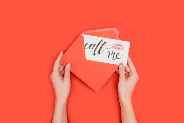 cropped shot of person holding red envelope and card with kiss mark and call me inscription isolated on red