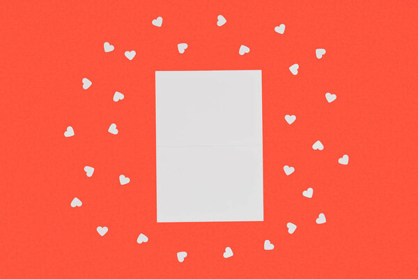 top view of blank white card and small hearts isolated on red