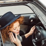 Hoge hoekmening van roodharige vrouw in zwarte hoed praten over smartphone tijdens de vergadering op stuurwiel in auto