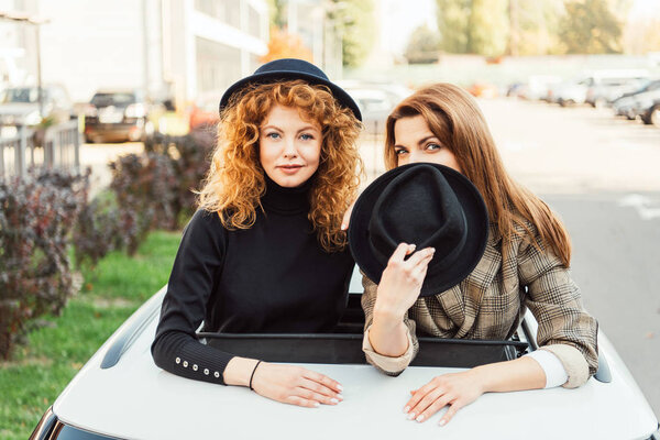 attractive fashionable women posing and leaning out from car hatchway at urban street