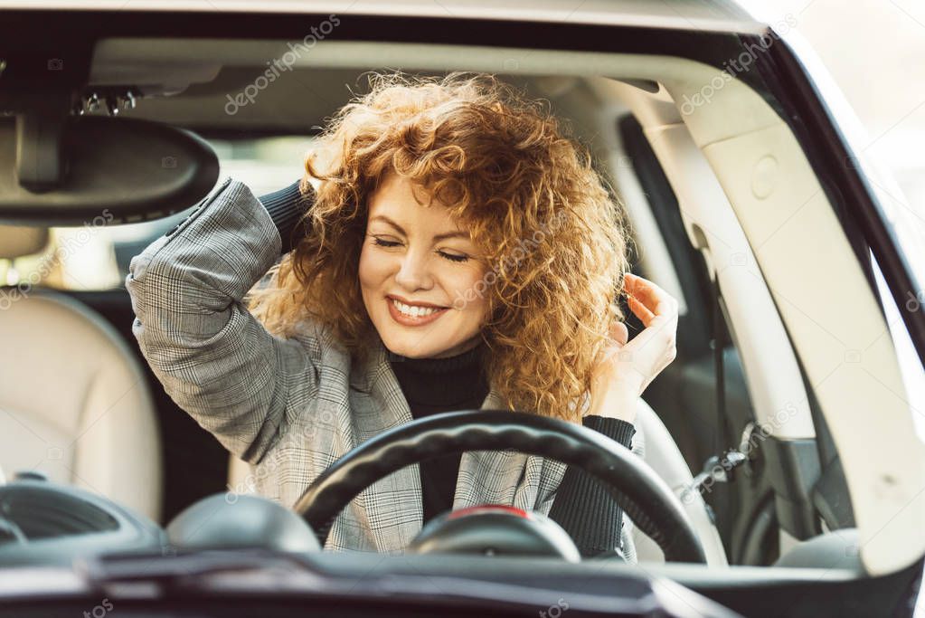 happy beautiful curly ginger woman with closed eyes sitting in car 