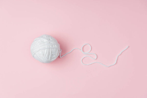 вид сверху на белый клубок пряжи для вязания на розовом фоне
