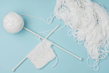 pembe zemin üzerinde beyaz iplik ve örme iğneler üstten görünüm