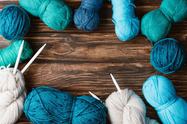 flat lay with arranged yarn clews and knitting needles on wooden surface