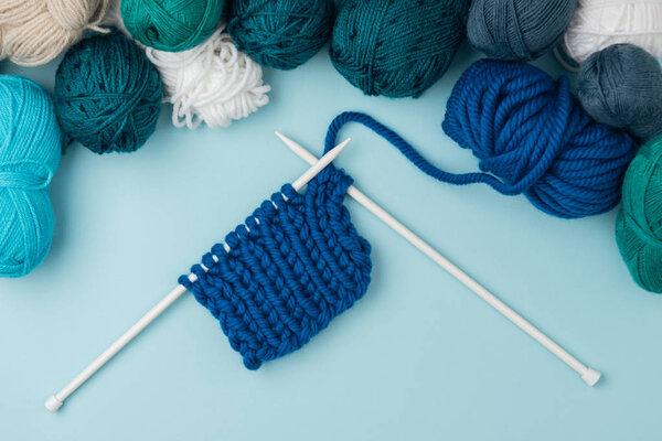 top view of arranged yarn clews and white knitting needles on blue background 