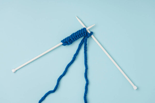 top view of blue yarn and white knitting needles on blue background 