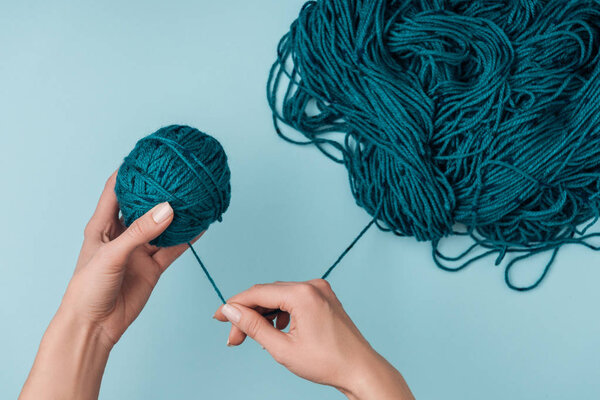 partial view of woman rolling yarn ball on blue background