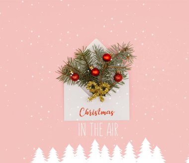 top view of white envelope with fir twigs and shiny christmas baubles isolated on pink with 