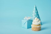 Partyhut, Geschenkbox und leckerer Cupcake auf blauem Hintergrund
