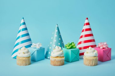 Colorful party caps,gifts and tasty cupcakes on blue background clipart