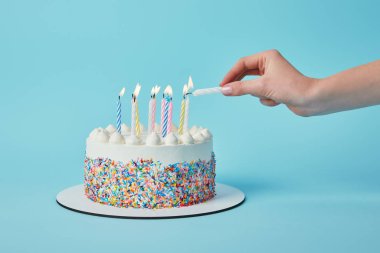 Partial view of woman lighting candles on birthday cake on blue background clipart