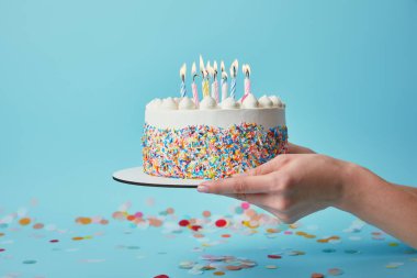 Partial view of woman holding birthday cake with candles on blue background with confetti clipart