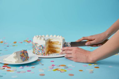 Partial view of woman cutting delicious cake on blue background clipart