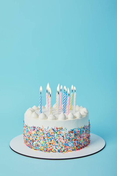 Вкусный праздничный торт с зажженными свечами на голубом фоне
