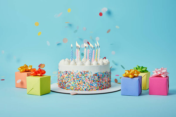 Вкусный торт со свечами, красочные подарки и конфетти на голубом фоне
