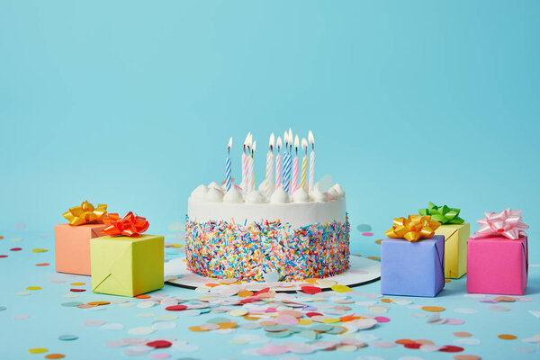 Вкусный торт со свечами, красочные подарки и конфетти на голубом фоне
