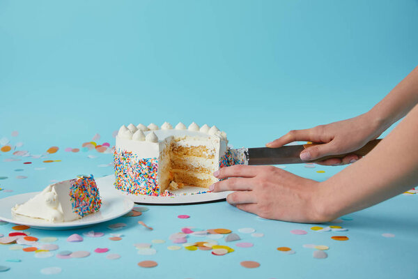 Partial view of woman cutting delicious cake on blue background