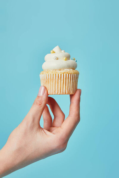 Cropped view of woman holding delicious cupcake on blue background