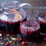 Homemade mulled wine with cranberries in glasses and teapot on table in kitchen