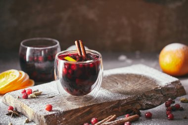 homemade mulled wine with cranberries, orange and cinnamon sticks on wooden stand in kitchen clipart
