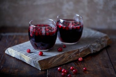 two glasses of tasty mulled wine with cranberries on wooden stand in kitchen clipart
