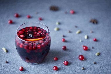 glass of tasty homemade mulled wine with cranberries and orange, scattered berries on tabletop in kitchen clipart
