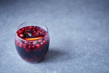 glass of tasty homemade mulled wine with cranberries and orange on grey tabletop in kitchen clipart