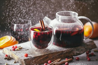 homemade mulled wine with cranberries in glasses and teapot with falling powdered sugar on table in kitchen clipart