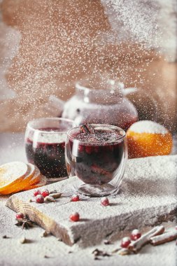 powdered sugar falling on two glasses of tasty mulled wine with cranberries on table in kitchen clipart