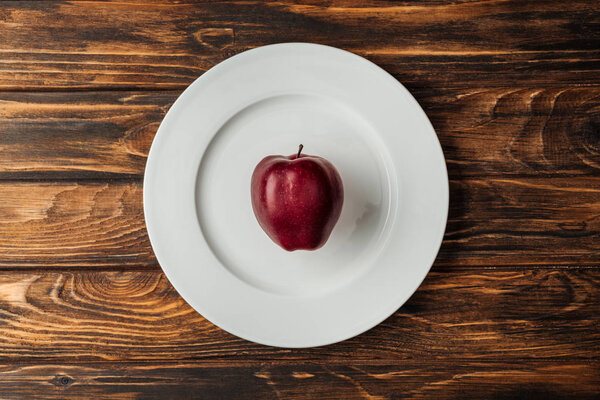 top view of white plate with red delicious apple on wooden table