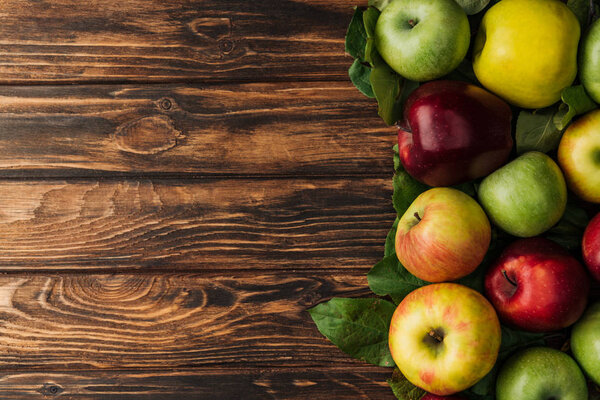 top view of ripe multicolored apples and leaves on wooden table