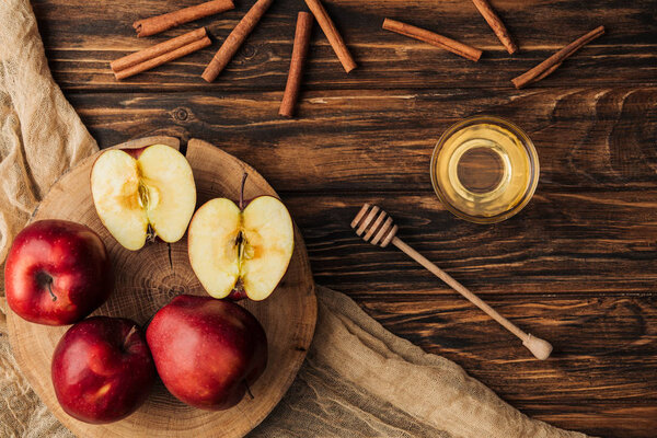 top view of red delicious apples, honey, cinnamon and fabric on wooden table