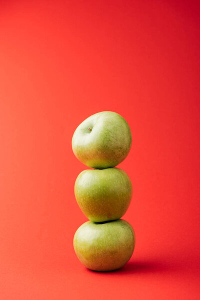 stack of three ripe green apples on red background
