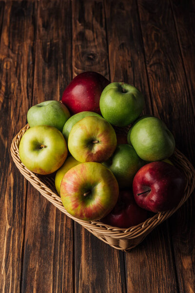 red, green and golden apples in wicker basket on rustic wooden table