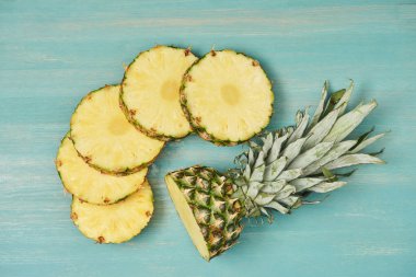 Turkuaz ahşap masa üzerinde kesme ananas yakınındaki dilimlenmiş ananas çevrelerin üstten görünüm