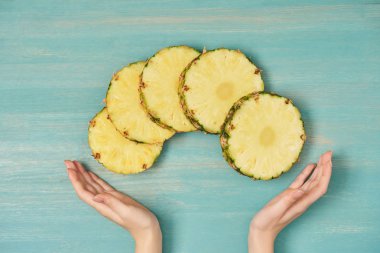 ananas dilimlenmiş daireler yakınındaki eller görünümünü turkuaz ahşap masa üzerinde kırpılmış