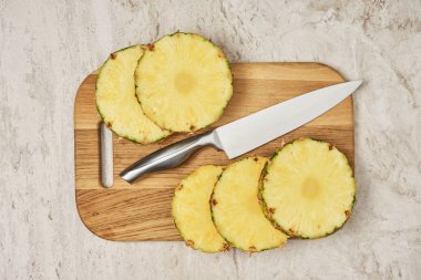 bıçak yakınındaki ahşap kesme tahtası üzerinde dilimlenmiş ananas çevrelerin üstten görünüm 