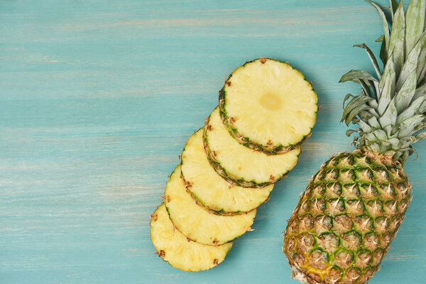 top view of sliced juicy circles near whole pineapple on turquoise wooden table